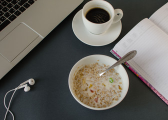 Breakfast before working. Office desk with bowl of granola with milk, coffee, laptop, headphones and notebook. flat lay top view concept