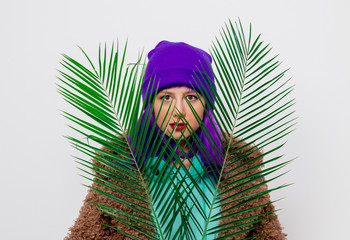 Beautiful young girl with purple hair in jacket with palm leaf on white background.
