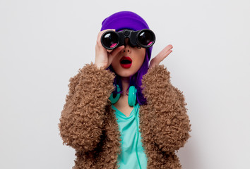 Beautiful young girl with purple hair in jacket looking in to binocular on white background.