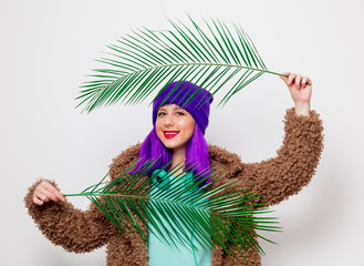 Beautiful young girl with purple hair in jacket with palm leaf on white background.