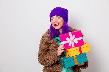 Beautiful young girl with purple hair in jacket with holiday gift boxes on white background.