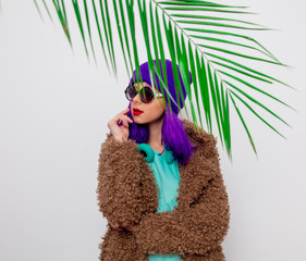 Beautiful young girl with purple hair in jacket with palm leaf on white background.
