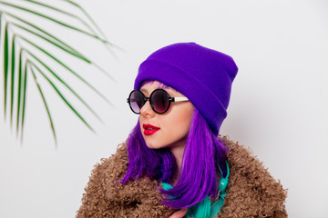Beautiful young girl with purple hair in jacket with palm leaf on white background.