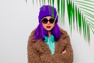 Beautiful young girl with purple hair in jacket with palm leaf on white background.