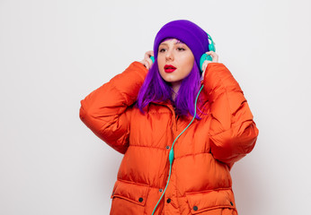 Beautiful young girl with purple hair and in orange jacket listen music in headphones on white background.
