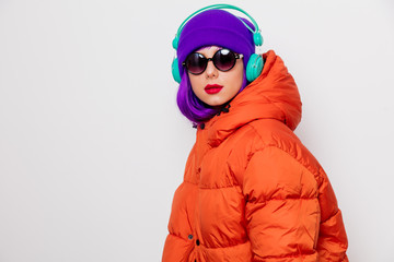 Beautiful young girl with purple hair and in orange jacket listen music in headphones on white...