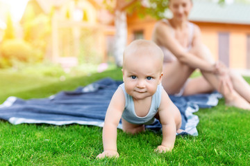 Portrait of cute little caucasian boy having fun in garden with mother. Child crawling on green...