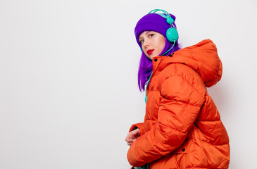 Beautiful young girl with purple hair and in orange jacket listen music in headphones on white background.