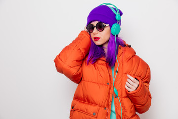 Beautiful young girl with purple hair and in orange jacket listen music in headphones on white background.
