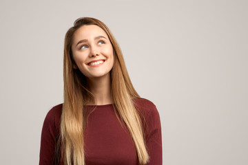 Obraz premium Intriguing young woman, looks mysteriously aside, has brilliant idea in mind. Fomale poses against white studio background with free space for your advertising content
