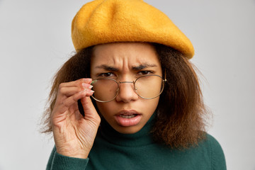 Angry dark haired woman has scrutinized look through spectacles, dissatisfied with something, poses...