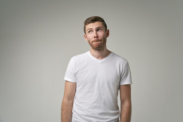 Pensive man looking to the side. Studio shot of doubtful guy, looks upwards, poses against white background with free space for your advertising content.