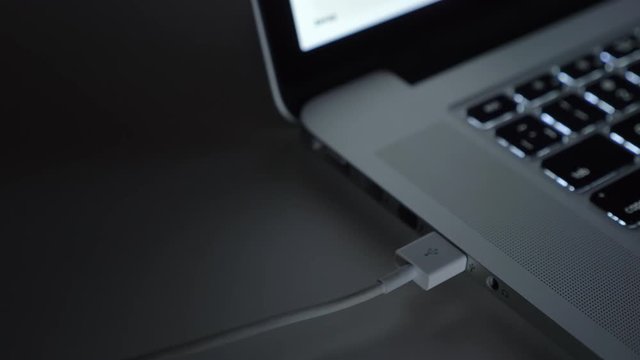 Close-up shot of male hand fastly inserting usb wire into laptop on black table background.