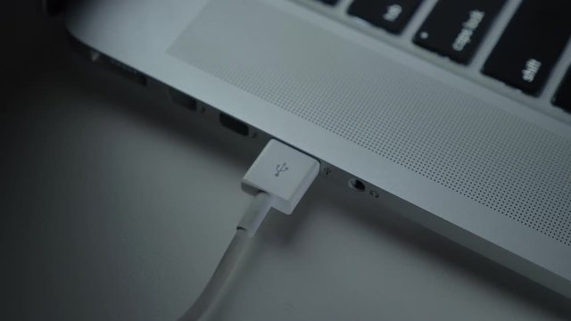 Close-up shot of hand fastly inserting white usb cable into laptop on black table background.