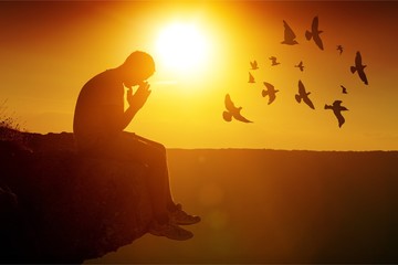 Young man pray outdoor on top of mountains in sunset