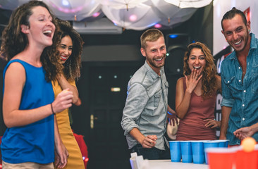 Happy friends playing beer pong in a cocktail bar - Young millennials people having fun doing party alcohol games at night pub - Friendship and youth lifestyle nightlife concept