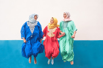 Happy muslim women jumping together outdoor - Arabian teen girls having fun in the city - concept of people,costume, culure and religion