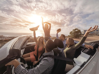 Happy friends with their hands up having fun in cabriolet car on vacation - Young people laughing...