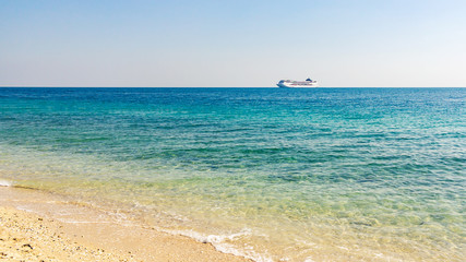 Turquoise sea with light ripples on the water and a large cruise liner on the horizon
