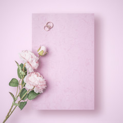 A romantic love letter that is yet to be written with wedding rings and rose on pink background. Flat lay image with copy space.