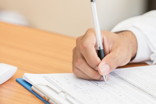 Healthcare Medical Expenses Concept, Hands Doctor's Writing And Working On Prescription Clipboard With Record Information Paper Folders On Desk In Hospital Or Clinic. Selective Focus