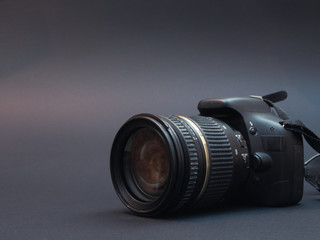 modern dslr photo camera on black dark background with zoom lens attached. low key image