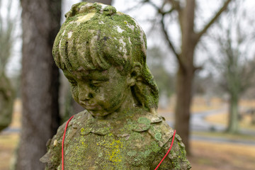 Moss covered statue of a girl wearing a Christmas bell necklace, on a grave in Greenwood Cemetery, Clarksville, Tennessee