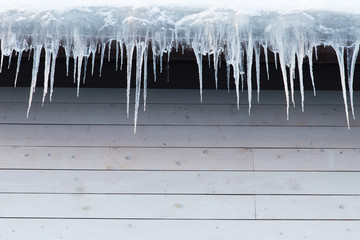 Building covered with icicles, closeup. Ice stalactite hanging from roof, copy space. Poor thermal insulation of the roof leads to the formation of icicles. Thaw, winter weather concept