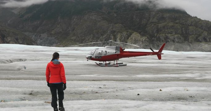 Woman walking on glacier in Alaska towards helicopter. Tourist or pilot visiting glacier on helicopter tour excursion. 59.94 FPS SLOW MOTION.