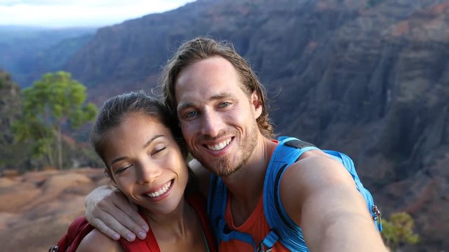 Couple taking selfie video having fun on hike on Hawaii. Woman and man in love taking candid selfportrait while on hiking travel in Waimea Canyon State Park, Kauai, Hawaii, USA.