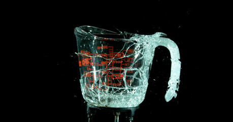 A Glass Measuring Cup Shattering, breaking, exploding into shards isolated on black. Moment of impact