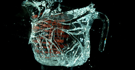 A Glass Measuring Cup Shattering, breaking, exploding into shards isolated on black. Cup still has form just shattered. 