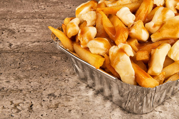 Partial close up on a poutine in a takeout container. Cooked with french fries, beef gravy and curd...