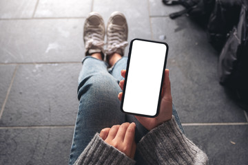 Top view mockup image of a woman holding black mobile phone with blank desktop screen while sitting on the floor with baggage
