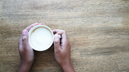 Human hand holding a cup of coffee wooden background and free space