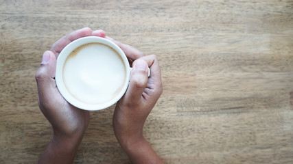 Human hand holding a cup of coffee wooden background and free space