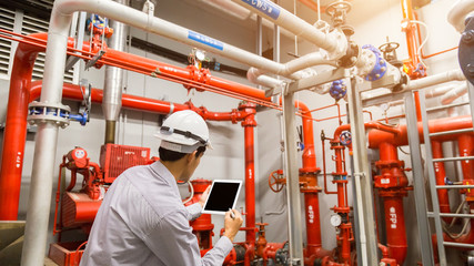 Engineer with tablet check red generator pump for water sprinkler piping and fire alarm control system. - obrazy, fototapety, plakaty