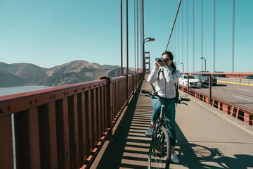 Cercles muraux Pont du Golden Gate Golden gate bridge biking lady sightseeing in San Francisco USA. Young female tourist on bike tour enjoying the view stop riding bicycle taking picture shooting photographing on sunny day in summer.
