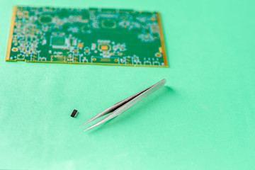 Tweezers, Computer chip and blurred small PCB-printed circuit board on green background. The...