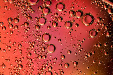 Macro shot of backlit liquid with small bubbles in it over colored background.