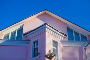 upper part of facade of two-story house of pink color with sloping roof against the blue sky