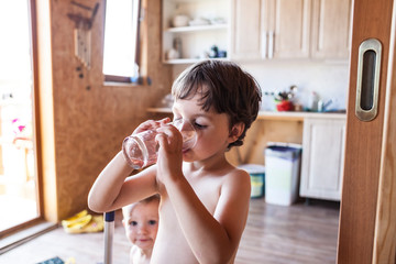 The boy drinks water from a glass.