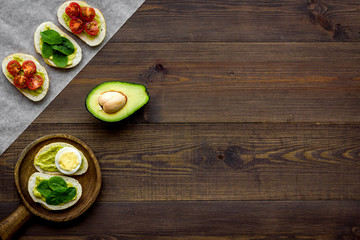 Fototapeta na wymiar Healthy snacks. Set of toasts with vegetables like avocado, guacamole, rocket, cherry tomatoes on dark wooden background top view copy space