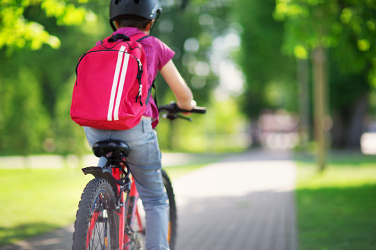 Child with rucksack riding on bike in the park near school