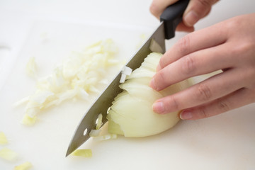白い背景にまな板で玉ねぎを女性の手でみじん切り