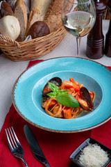 Italian cuisine. Pasta with seafood, tomatoes and cheese in a blue, a fork and a knife on a light background.