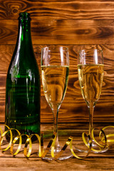 Bottle of champagne and two wineglasses decorated with golden ribbon on wooden table