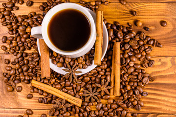 Cup of hot coffee, star anise, cinnamon sticks and scattered coffee beans on wooden table. Top view