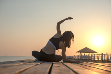 sport woman in practice of exercise on wooden bridge at sunset, enjoy music while workout on the pier jetty in the sea