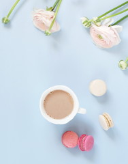 Flowers background. Pastel colors pink ranunkulus flowers, cup of cocoa, macaroni cakes , notebook on pale blue background. Top view.Copy space